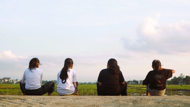 Group of young women sitting together and looking at the rural landscape at sunset.