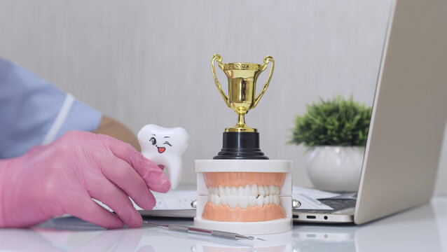 Pediatric dentistry success concept showing a dentist holding a cute smiling tooth character next to a golden trophy.