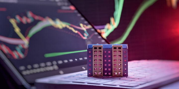 Digital property trading and mortgage rates. Toy apartment house on computer keyboard against blurred stock market graphs.