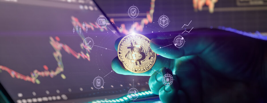 Futuristic crypto investment concept. Investor holding golden Bitcoin over laptop with fintech hologram interface and stock market graphs.