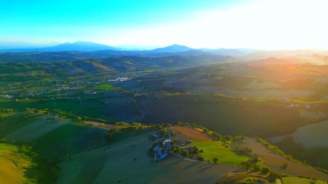 Splendid aerial pullback shot from Monterubbiano, spiritual light from the afternoon sun imbuing the hillscapes with soothing qualities in the hazy atmospheres of the Marche countryside, mountains