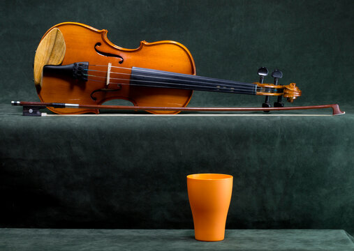 Still life with a violin, bow, and orange cup on a green background.