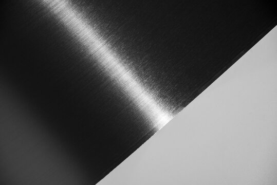 Curved black stainless steel sheet with metallic glare isolated on white background.