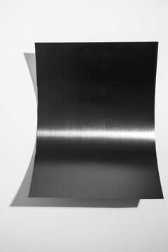 Curved black stainless steel sheet with metallic glare isolated on white background.