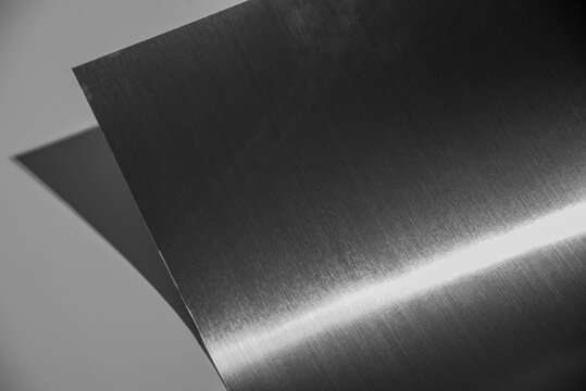 Curved black stainless steel sheet with metallic glare isolated on white background.