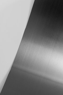 Curved black stainless steel sheet with metallic glare isolated on white background.