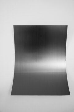Curved black stainless steel sheet with metallic glare isolated on white background.