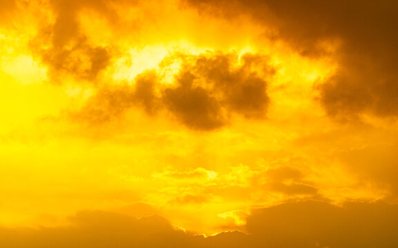 Dramatic golden sky with dark clouds illuminated by intense sun rays. High resolution natural background for design, nature and weather themes.