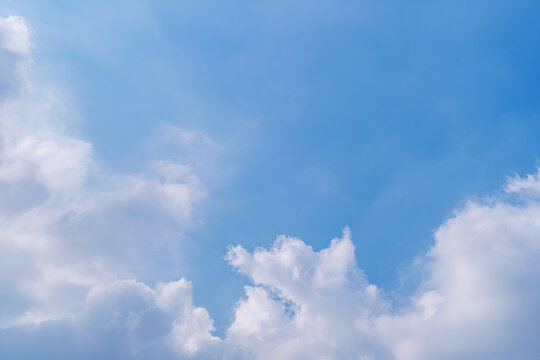 Blue sky with fluffy white clouds under natural daylight. Clean high resolution background with large copy space for graphic design and advertising.