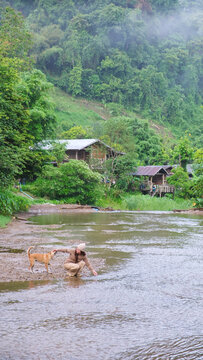 Vertical of a woman playing with a dog by the river in rural village