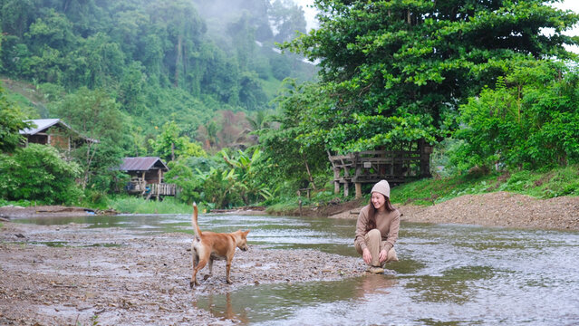 A woman playing with a dog by the river in rural village