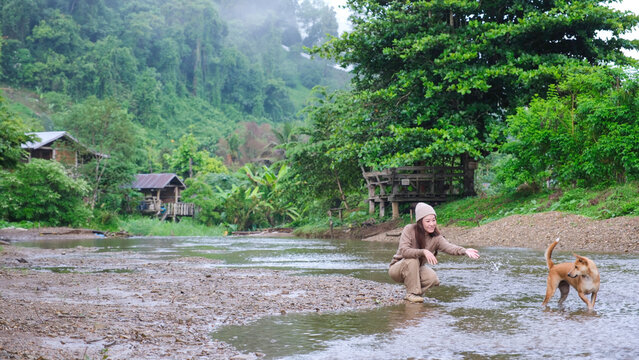 A woman playing with a dog by the river in rural village