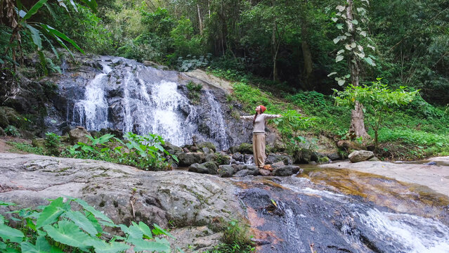 A woman opening arms and relaxing by the waterfall in the forest