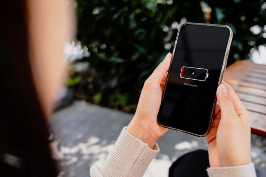 Close-up of a woman holding a smartphone showing a low battery warning at home. Ideal for mobile charging, battery life, technology, productivity and lifestyle concepts.
