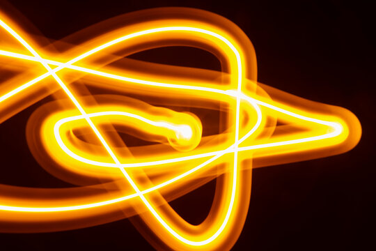 Abstract long exposure of tangled yellow glowing light trails over dark background.