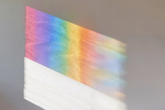 Reflets arc-en-ciel projet&eacute;s par la lumi&egrave;re naturelle sur un mur blanc, jeu de couleurs prismatiques, fond abstrait lumineux &eacute;voquant la diversit&eacute;, l&rsquo;espoir, la cr&eacute;ativit&eacute; et le spectre lumineux