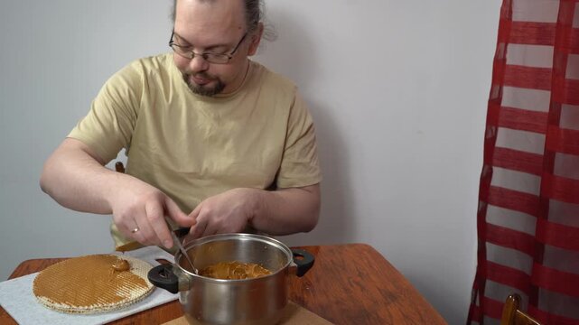 Spread cream on the cakes. Man is making a waffle cake with condensed milk. Cooking food at home.