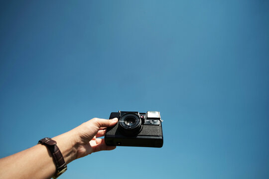Close up woman hand holding vintage black film camera with blue sky with sunny day. Copy space