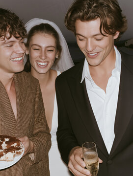 Three friends laughing with cake and champagne at a formal celebration. Ideal for wedding reception and party campaigns.