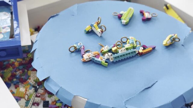 Small colorful handmade toy keychains scattered on a blue paper circle, seen in a close-up craft setting with other pieces in the background.