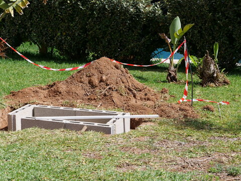 A pile of soil, concrete blocks, and safety tape marking an active garden digging project.