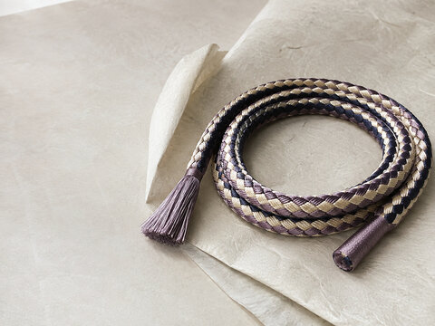 Traditional Round Kumihimo Braided Cord with Diamond Chevron Pattern Coiled on Folded Washi Paper, Traditional Japanese Kimono Accessory Background with Copy Space