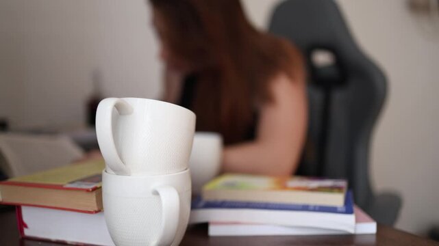 Two empty coffee cups sit on the desk while a young woman keeps studying showing how long hours of learning often rely on repeated caffeine refills to stay focused