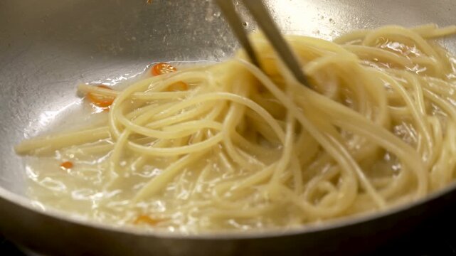 The chef saut&eacute;s the spaghetti in a pan to finish cooking it
