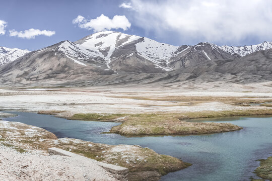 Clear-water rivers and lakes in a mountain valley, pastures and green grassy fields set against mountain ranges and snow-capped, glacier-clad peaks&mdash;a scenic landscape background