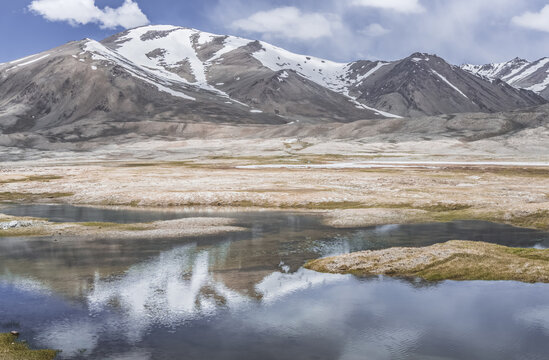 Clear-water rivers and lakes in a mountain valley, pastures and green grassy fields set against mountain ranges and snow-capped, glacier-clad peaks&mdash;a scenic landscape background