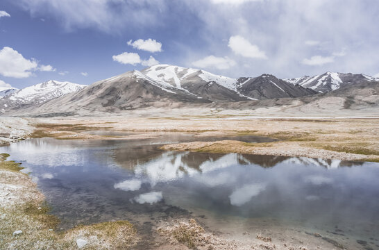 Clear-water rivers and lakes in a mountain valley, pastures and green grassy fields set against mountain ranges and snow-capped, glacier-clad peaks&mdash;a scenic landscape background