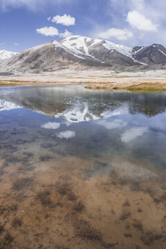 Clear-water rivers and lakes in a mountain valley, pastures and green grassy fields set against mountain ranges and snow-capped, glacier-clad peaks&mdash;a scenic landscape background