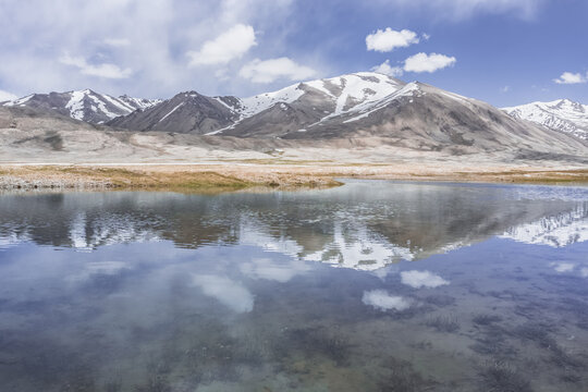 Clear-water rivers and lakes in a mountain valley, pastures and green grassy fields set against mountain ranges and snow-capped, glacier-clad peaks&mdash;a scenic landscape background