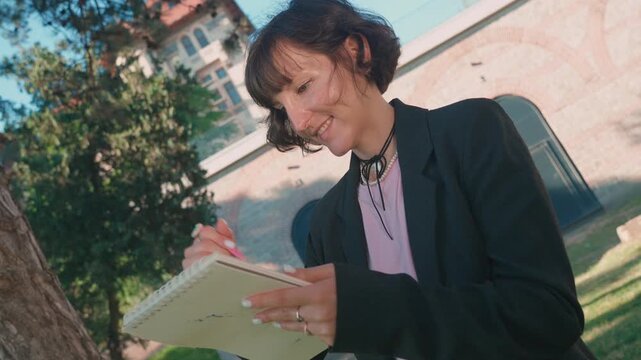 Female artist sketching in notebook with pink pencil outdoors