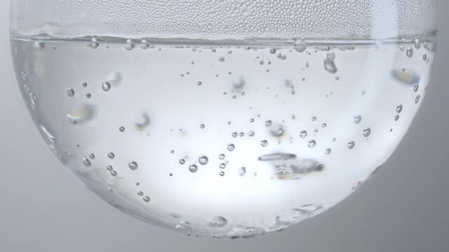 Macro video of clear liquid with rising air bubbles and water condensation in round glass flask, science lab boiling experiment, cosmetic skincare serum background for commercial advertising