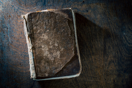 Ancient weathered book on dark rustic wooden table, closeup. Top view of an old shabby book with damaged cover lying on scratched wood background, symbolizing history, wisdom, and literature
