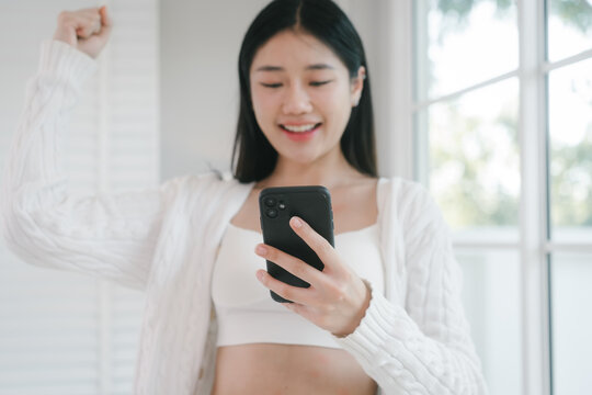 Smiling young woman in white clothes talking on a phone by a bright window at home, creating a calm, fresh, and modern lifestyle scene with natural light.