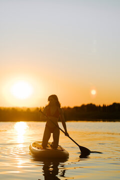 Woman kneeling on a paddle board in the lake while enjoying the warm golden light of the sunset