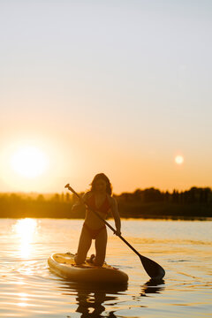 Woman paddling on a stand up paddle board on calm water during a bright and peaceful sunset session