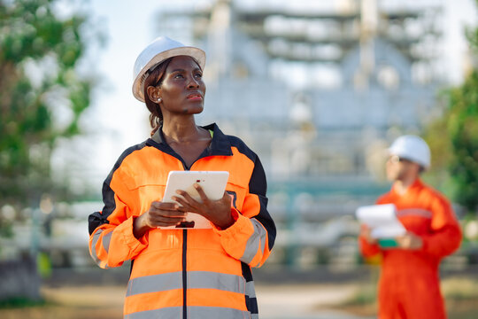 Industrial safety engineer evaluating refinery equipment with tablet during field inspection. Engineering assessment, maintenance planning, digital workflow and industrial operations.