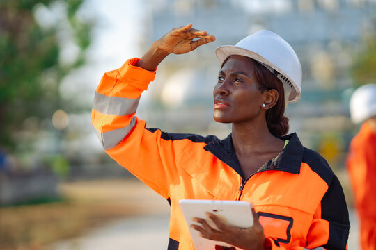 Industrial engineer checking production facility while shielding eyes from sunlight during site inspection. Equipment monitoring, safety management, engineering review and plant operations.