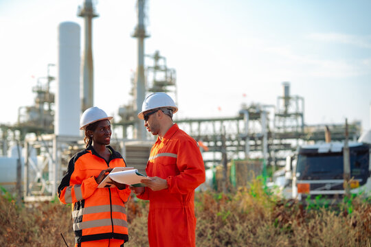 Maintenance engineers reviewing inspection documents and digital tablet at industrial processing plant. Engineering teamwork, equipment assessment, preventive maintenance and operational efficiency.