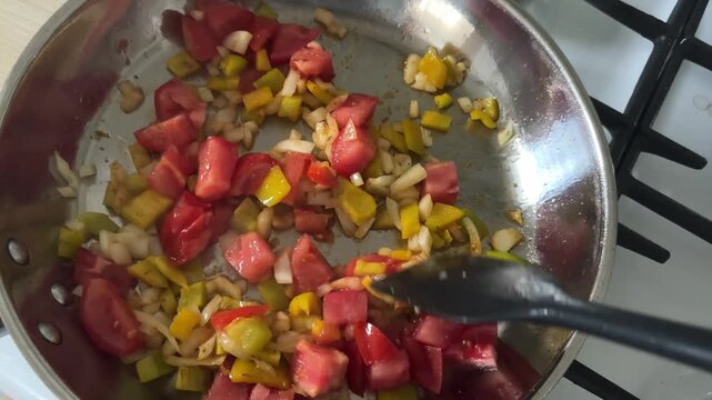 Cooking traditional shakshuka with frying tomatoes, onions and bell peppers in a heavy metal skillet on the stove