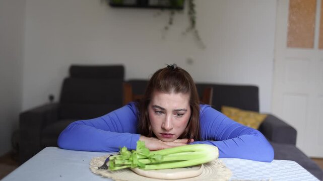 Young woman stares at untouched celery while obsessive calorie thoughts drain her motivation showing emotional burden of restrictive eating and food anxiety daily