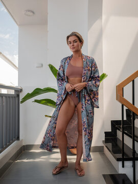 Elegant woman wearing luxury kimono robe over  swimsuit in modern tropical villa