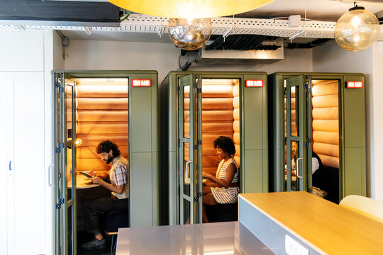 Diverse business professionals using acoustic booths for focused work, productivity, and privacy in a shared coworking space