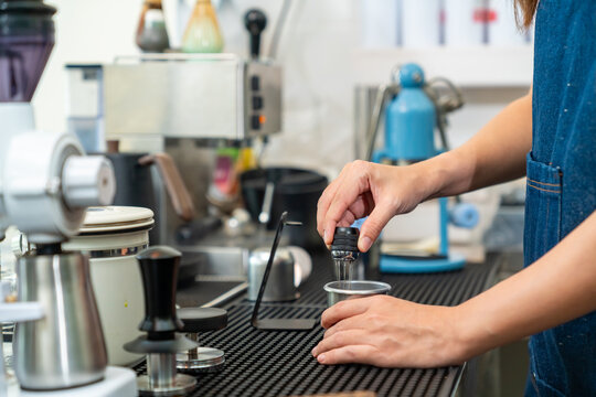Small business entrepreneur coffee shop cafe restaurant. Asian woman barista using manual espresso maker making freshly brewed coffee on bar counter. Waitress serving beverage drink to customer.