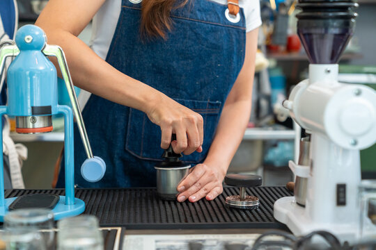 Small business entrepreneur coffee shop cafe restaurant. Asian woman barista using manual espresso maker making freshly brewed coffee on bar counter. Waitress serving beverage drink to customer.