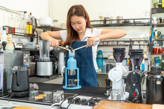Small business entrepreneur coffee shop cafe restaurant. Asian woman barista using manual espresso maker making freshly brewed coffee on bar counter. Waitress serving beverage drink to customer.