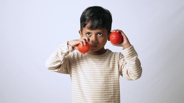 Indian boy holding oranges. Cute child eating healthy fruit against a white background.